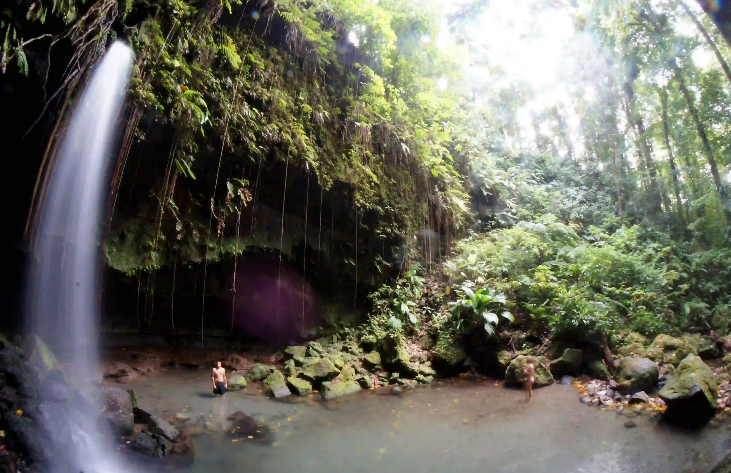 Travel guide to Dominica featuring a lush emerald rainforest river canyon leading to a cascading waterfall pool