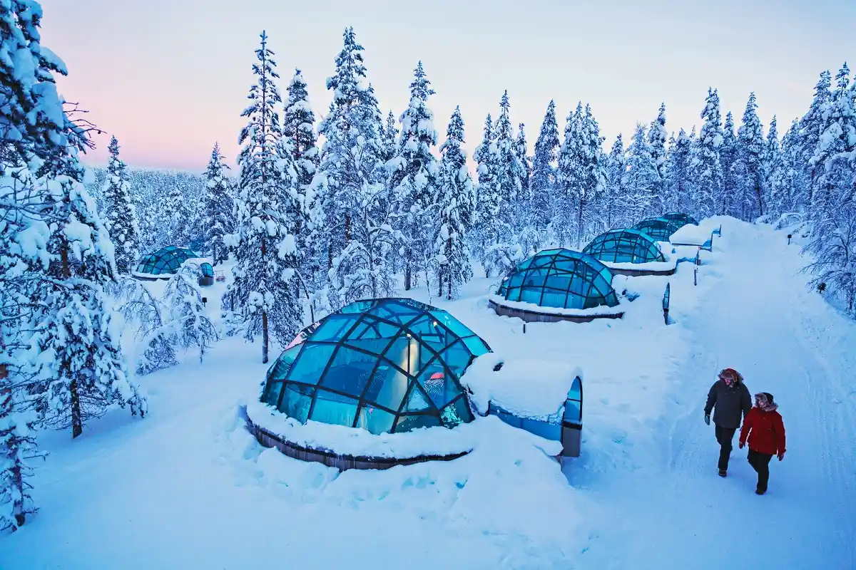 Travel guide to Finland featuring a cozy glass igloo hotel set in a snow-covered pine forest under the glowing Northern Lights in Lapland