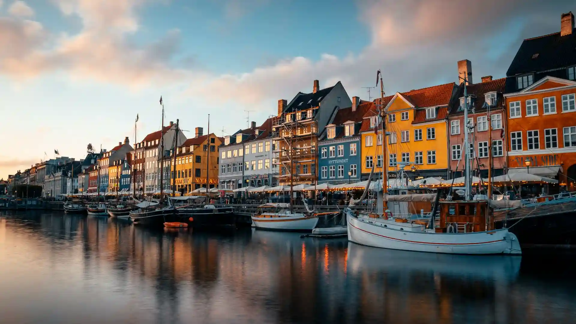 Travel guide to Denmark featuring the colorful historic gabled townhouses and wooden ships along Nyhavn canal in Copenhagen