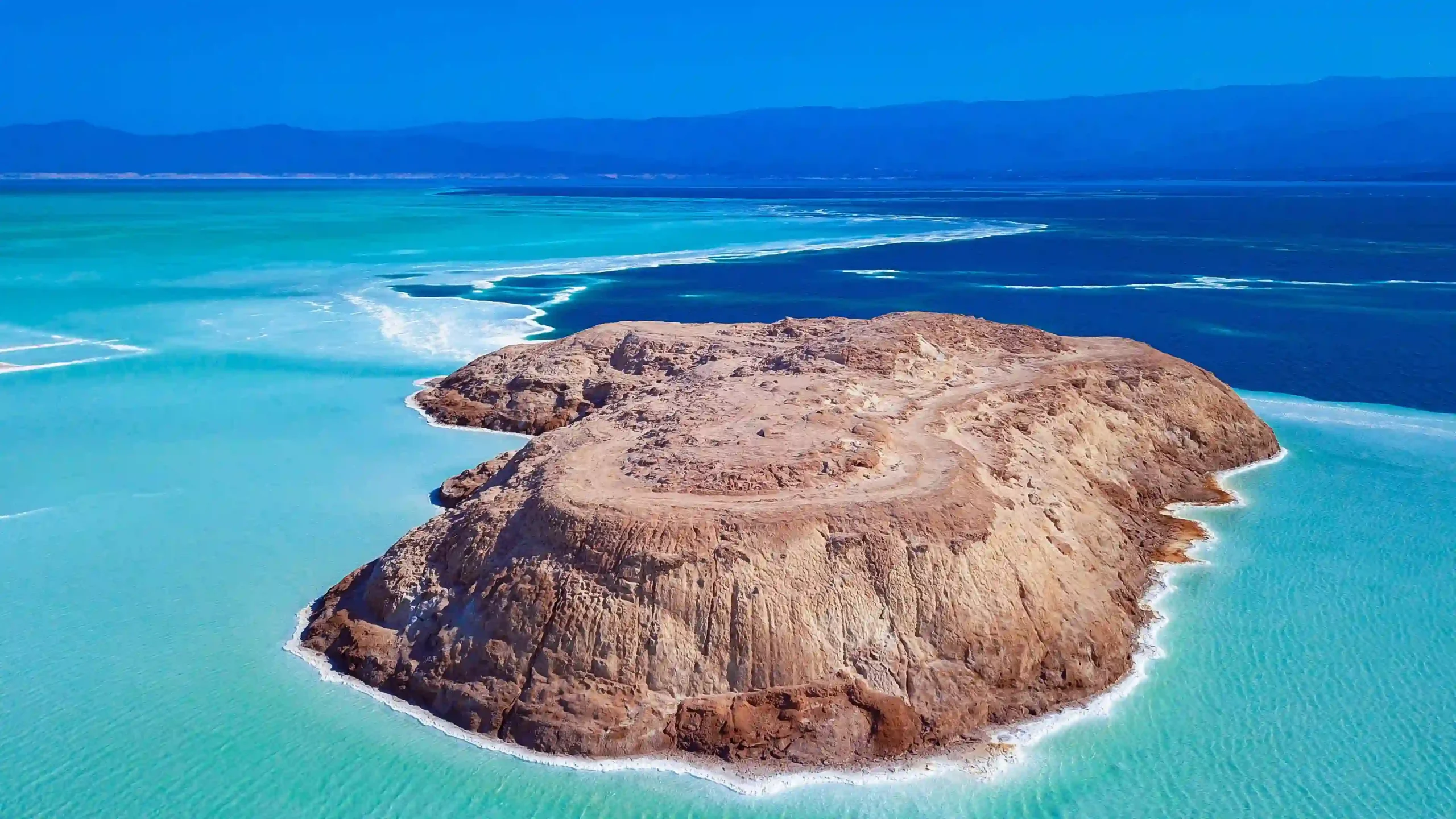 Travel guide to Djibouti featuring the turquoise salt waters and white salt shorelines of Lake Assal surrounded by volcanic hills