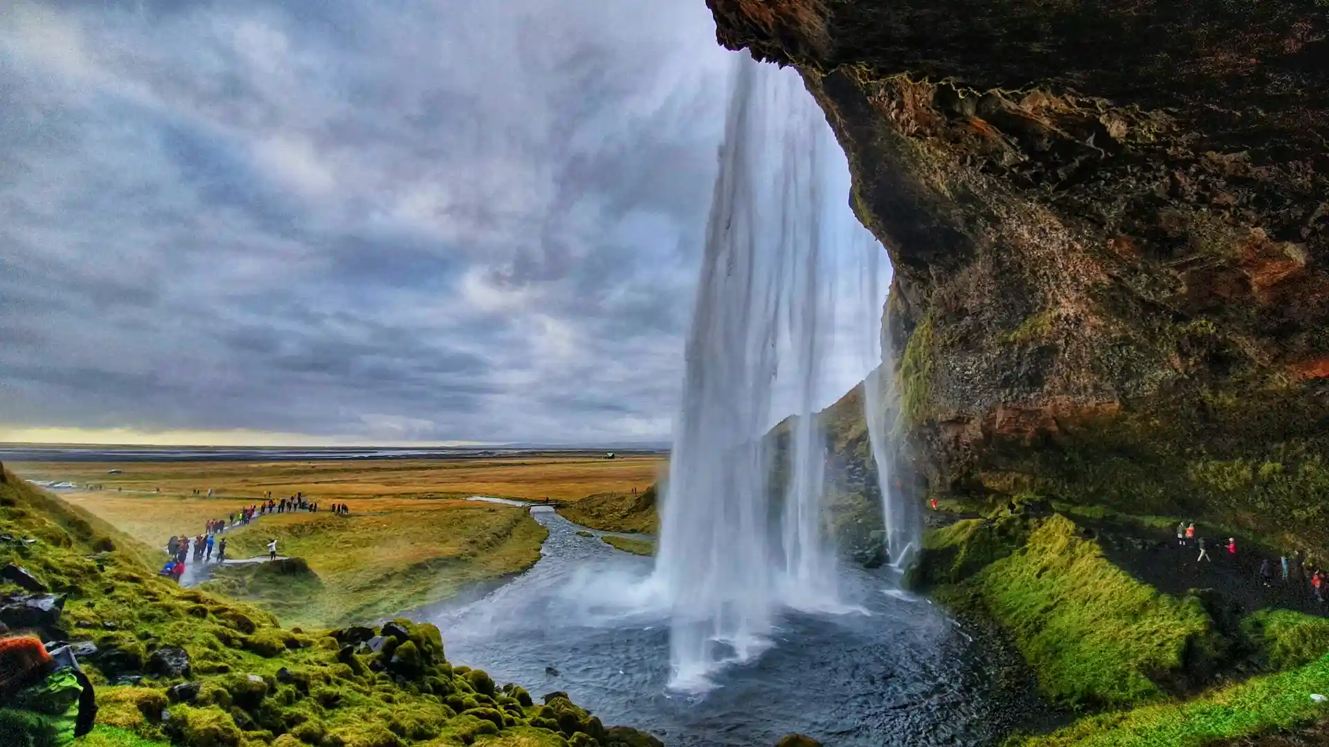 Travel guide to Iceland featuring Seljalandsfoss waterfall cascading over a cliff surrounded by green landscapes